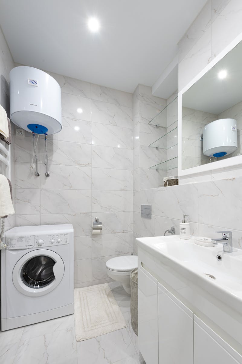 Emergency Boiler Repairs London: Your 24/7 Heating Lifesaver 1 A sleek white bathroom featuring a washing machine, sink, and boiler.